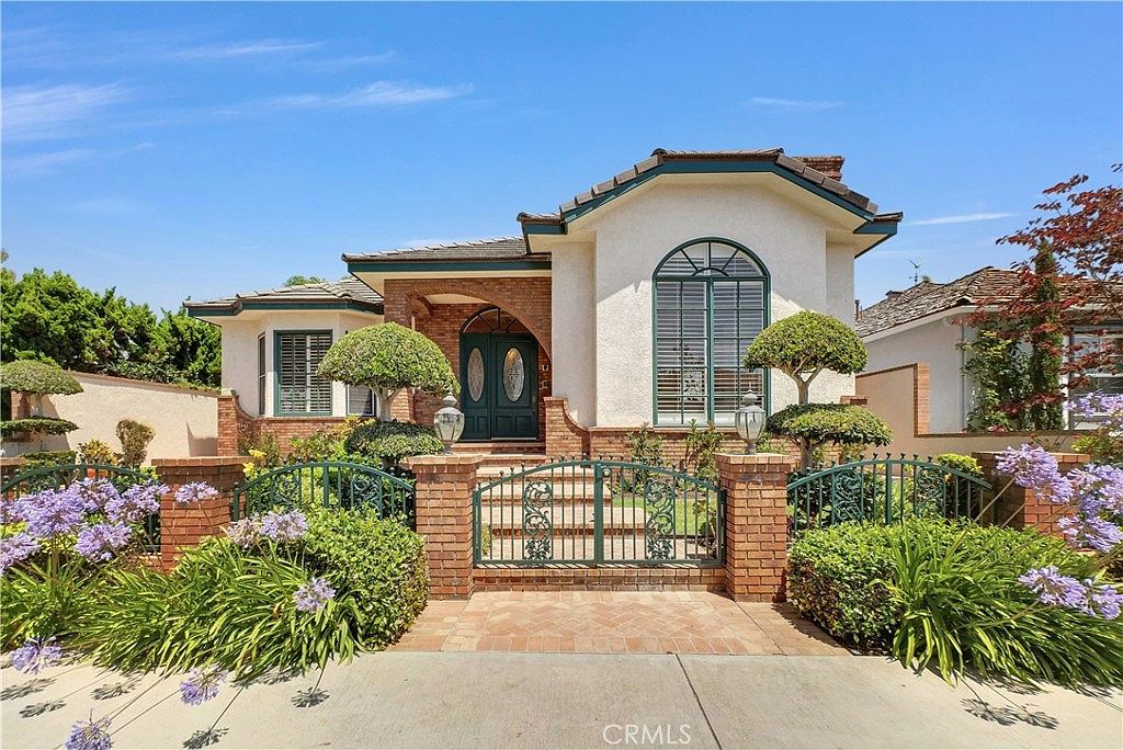 Front elevation of 236 Belmont Ave centered between wrought-iron gates, with topiary, purple agapanthus blooms, and an arched teal-trimmed entry under a blue sky