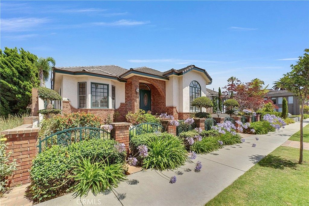 Sidewalk-angle view of the front of 236 Belmont Ave with mature gardens of agapanthus and small palms running along the street, the home framed on its corner of Belmont Avenue