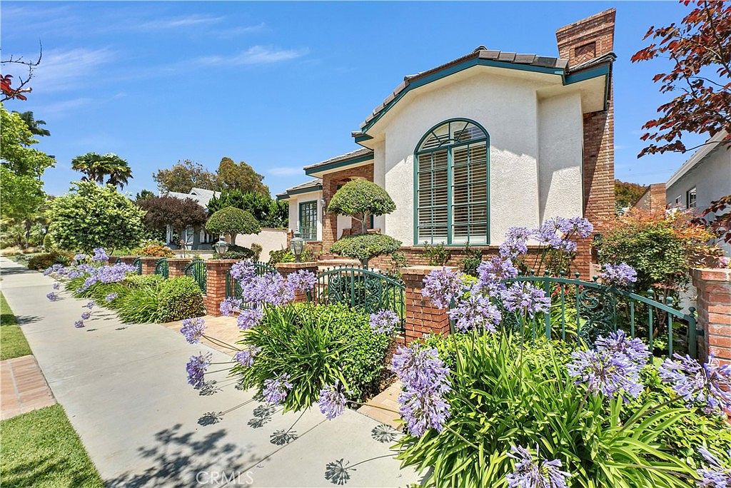 Side-angle view of the residence dense with purple agapanthus in bloom along the property line, with topiary and an arched second-story window catching afternoon light