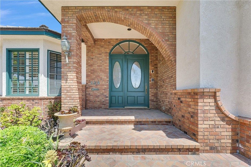A close-up of the front entry: a brick arch over a teal double door with oval inset glass, a small lantern sconce to the side, brick steps below