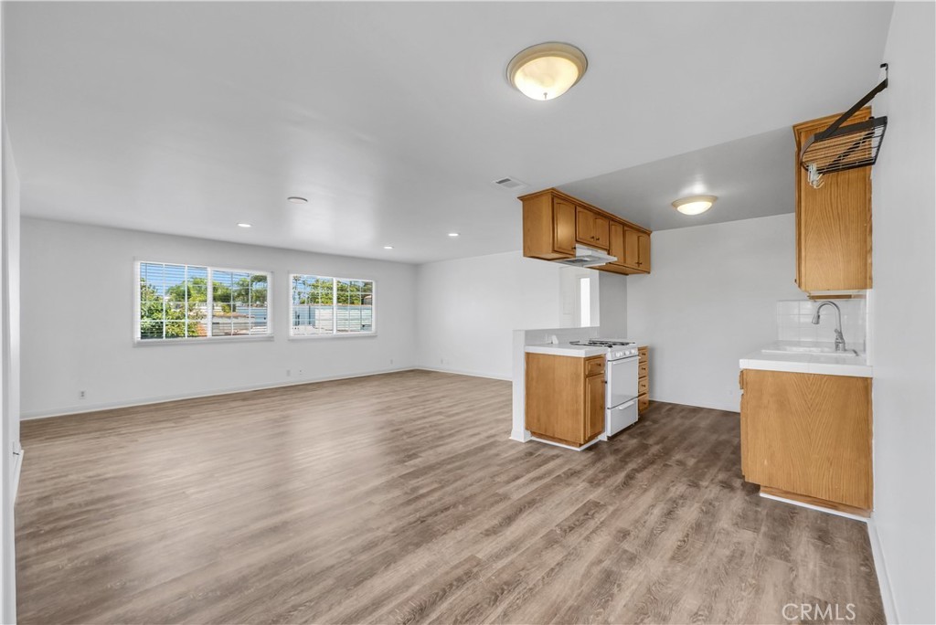 The upper guest unit above the four-car garage, an open studio-style great room and kitchenette with new wide-plank flooring, two windows looking onto the street, a small kitchen with a gas range, oak cabinetry and an overhead bin rack